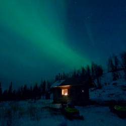 Aurora borealis at night near a snowy cabin