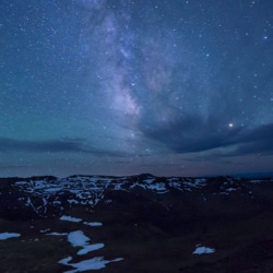 A clear sky of stars among a snowy, rock ladden area